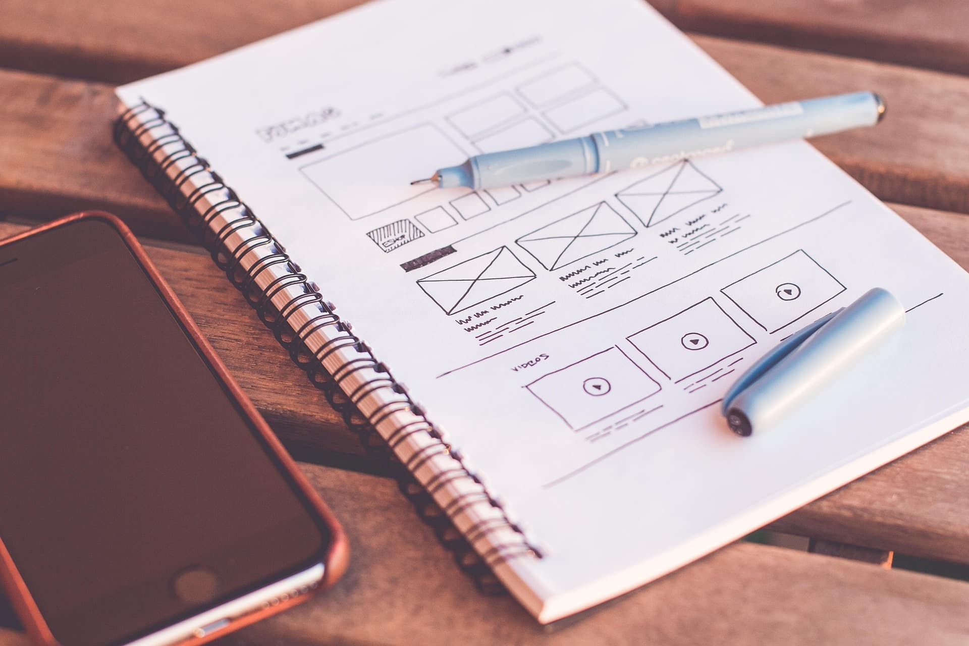 Hand-drawn website wireframes in a notebook beside a phone